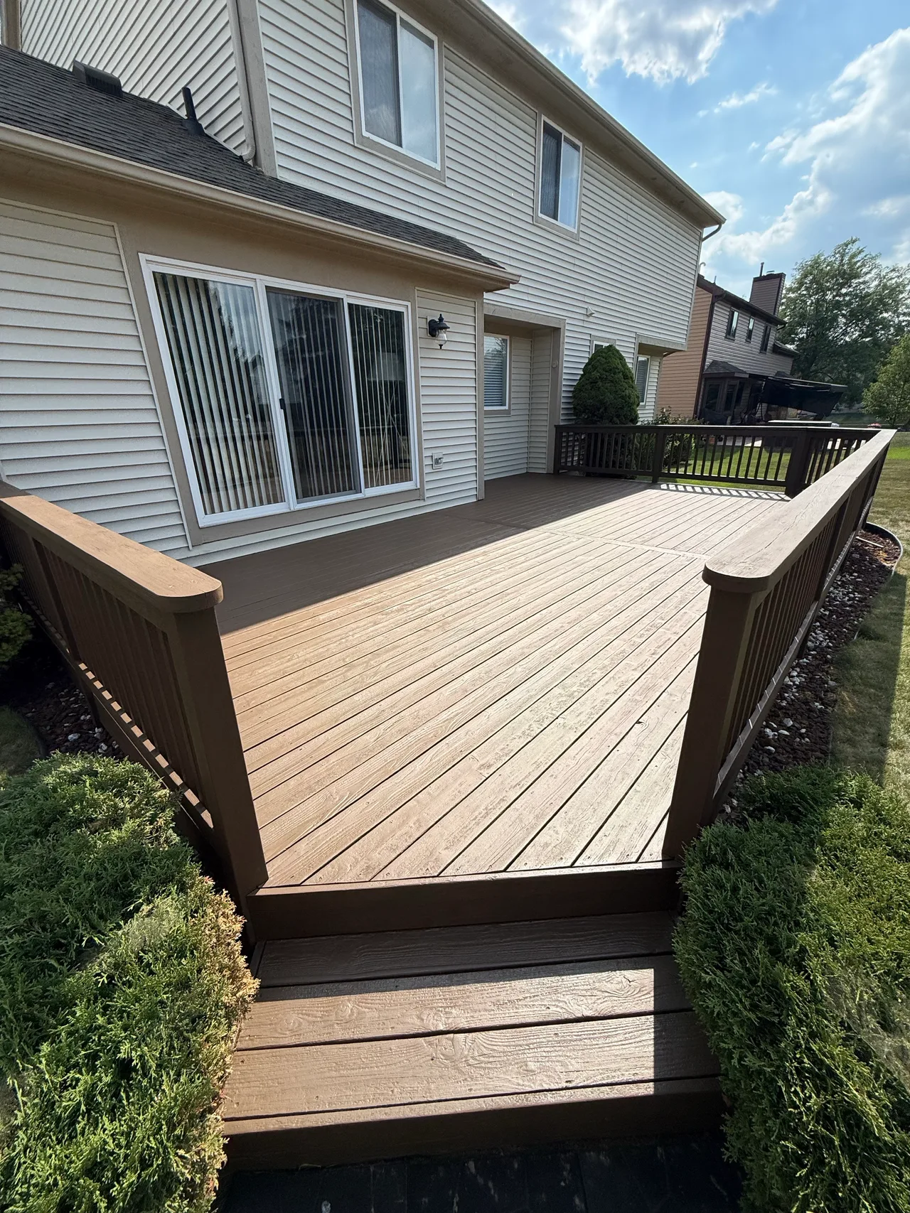 Brown-finished wood deck, rounded railings and entry steps beside a house