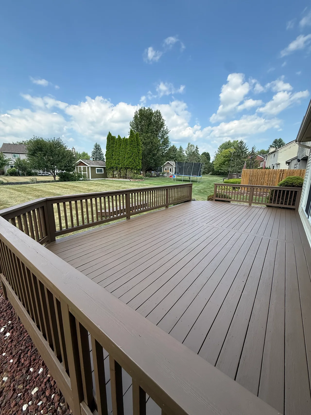 Deck boards and rails with a uniform gray-brown finish overlooking a backyard