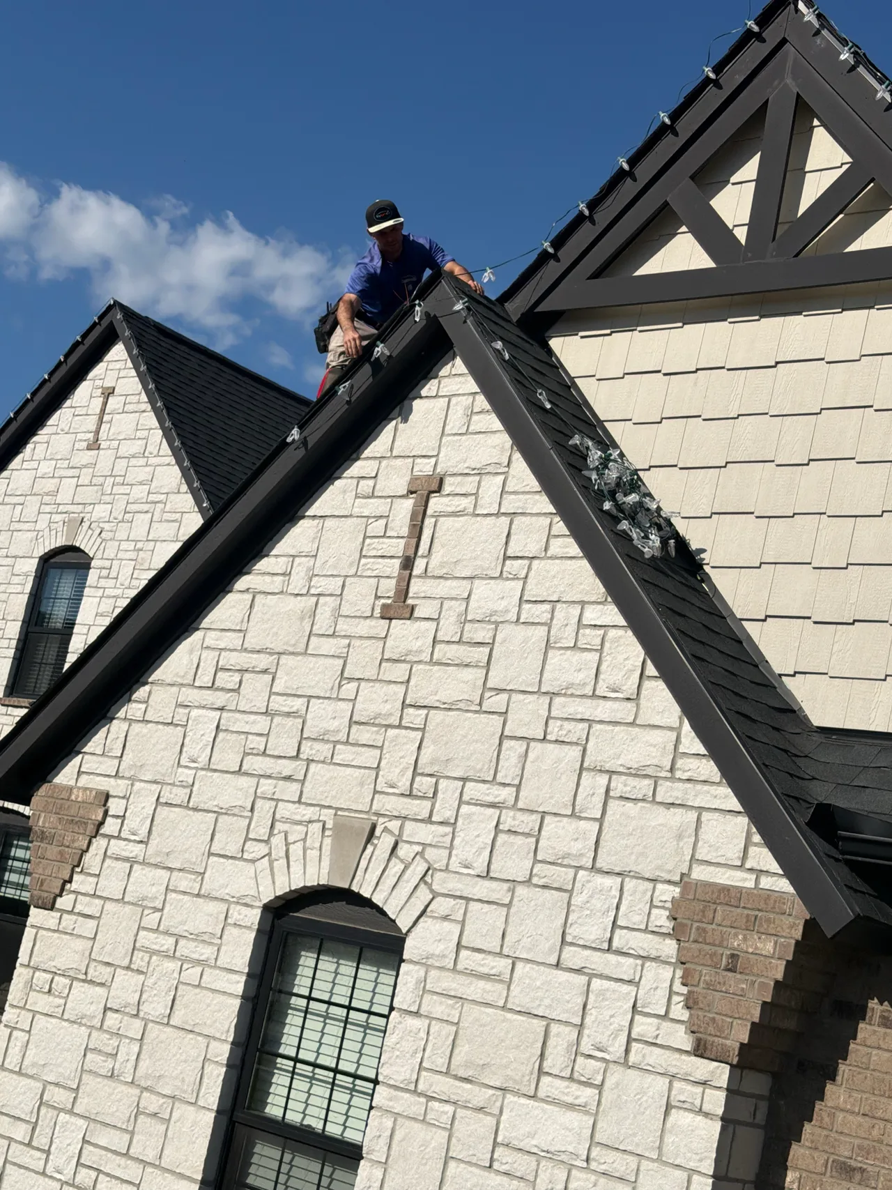 Installer working on holiday light strands along a gabled roofline