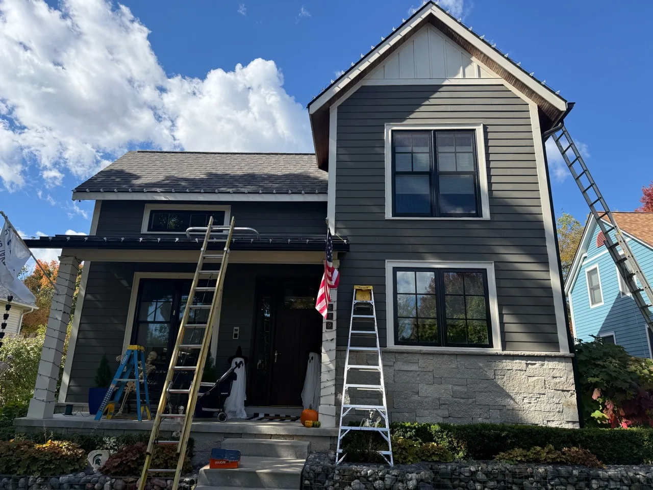 Daytime holiday-light installation along a home's rooflines with ladders set up